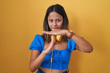 Hispanic young woman standing over yellow background doing time out gesture with hands, frustrated...