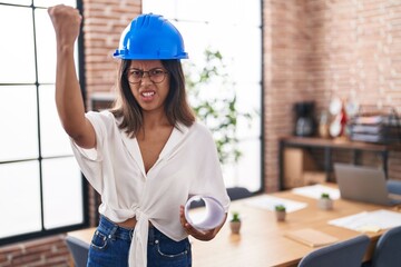 Hispanic young woman wearing architect hardhat at office annoyed and frustrated shouting with...