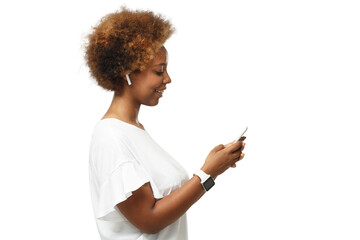 Side portrait of young african american woman surfing using mobile phone, listening to music via white wireless earphones