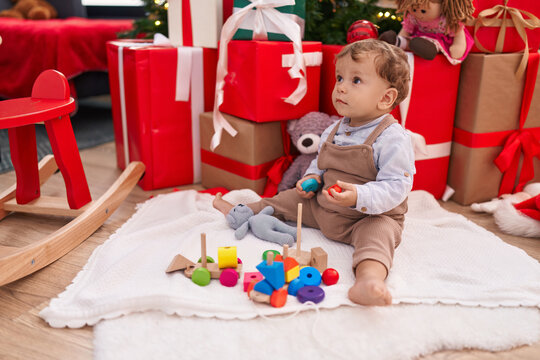 Adorable blond toddler playing with toys sitting on floor by christmas gifts at home