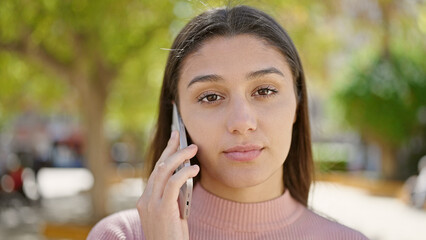 Young beautiful hispanic woman talking on smartphone with serious expression at park