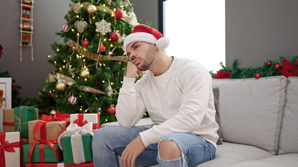 Obraz na płótnie Canvas Young hispanic man wearing christmas hat looking upset at home