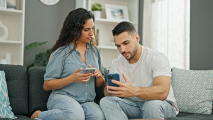 Man and woman couple using smartphones sitting on sofa at home - obrazy, fototapety, plakaty