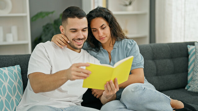 Man and woman couple reading book sitting on sofa at home