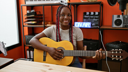 Smiling african american woman plays a classic melody on her guitar indoor. exceptional musician...