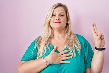Caucasian plus size woman standing over pink background smiling swearing with hand on chest and...