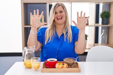 Caucasian plus size woman eating breakfast at home showing and pointing up with fingers number ten while smiling confident and happy.