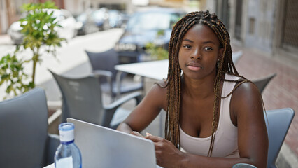 African american woman using laptop sitting on table at coffee shop terrace