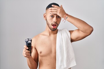 Young hispanic man holding electric razor stressed and frustrated with hand on head, surprised and...