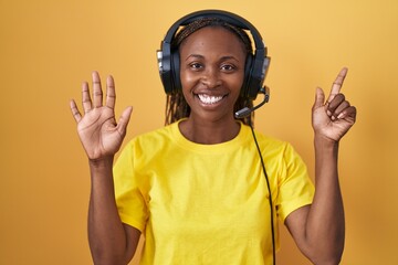 African american woman listening to music using headphones showing and pointing up with fingers number seven while smiling confident and happy.