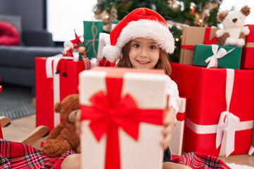 Obraz na płótnie Canvas Adorable hispanic girl holding christmas gift sitting on floor at home