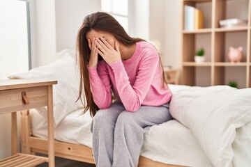 Young beautiful hispanic woman stressed sitting on bed at bedroom