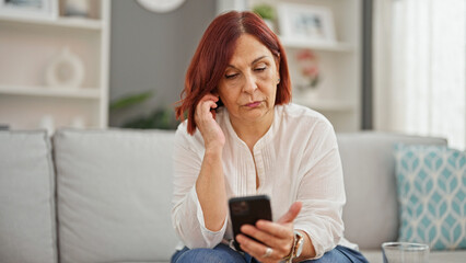 Middle age woman using smartphone with serious expression at home - obrazy, fototapety, plakaty