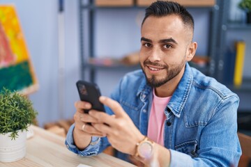 Young hispanic man artist using smartphone drawing at art studio