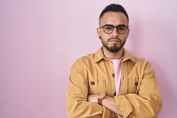 Young hispanic man standing over pink background skeptic and nervous, disapproving expression on face with crossed arms. negative person.