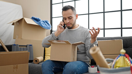 Hispanic man unpacking cardboard box speaking on the phone complaining at new home