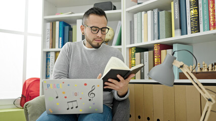 Hispanic man student reading book using the laptop at library university