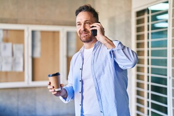 Young caucasian man talking on the smartphone drinking coffee at street