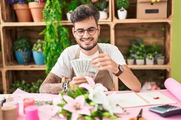 Young hispanic man florist smiling confident counting dollars at flower shop