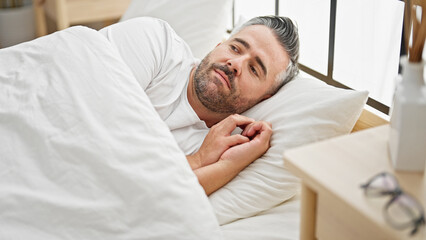 Fototapeta premium Grey-haired man lying on bed with serious expression at bedroom