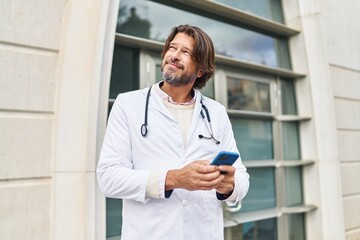 Middle age man doctor smiling confident using smartphone at hospital