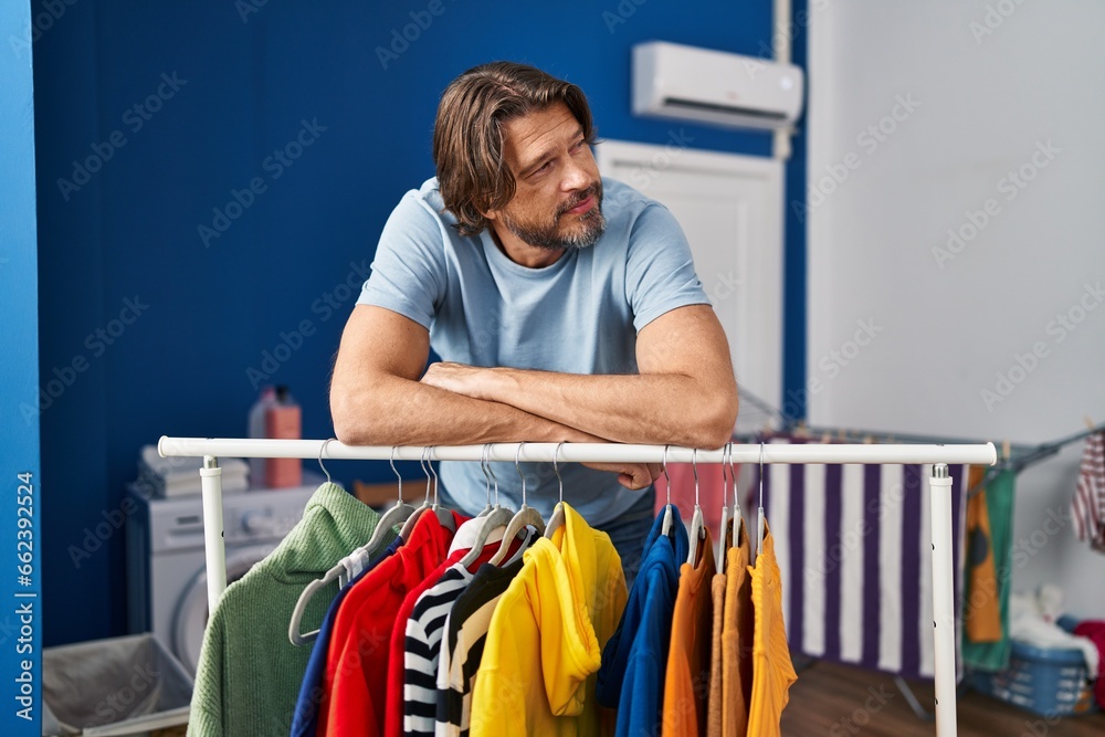 Wall mural Middle age man smiling confident leaning on clothes rack at laundry room - Wall murals