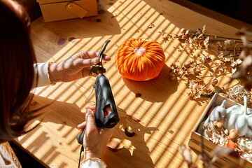 Woman making orange velvet fabric pumpkin. Autumn decoration with handmade textile pumpkin on wooden table. Fall vibes. Thanksgiving decor.