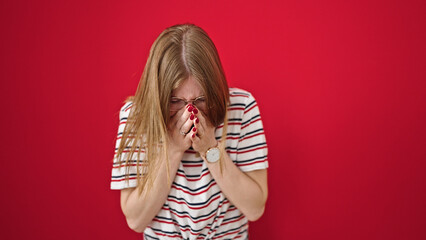 Young blonde woman sneezing over isolated red background