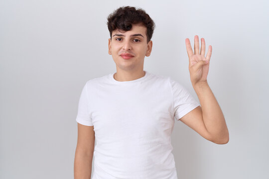 Young non binary man wearing casual white t shirt showing and pointing up with fingers number four while smiling confident and happy.