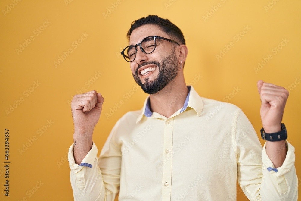 Canvas Prints Hispanic young man wearing business clothes and glasses celebrating surprised and amazed for success with arms raised and eyes closed. winner concept.