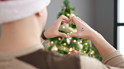Young arab man doing heart gesture standing by christmas tree at home