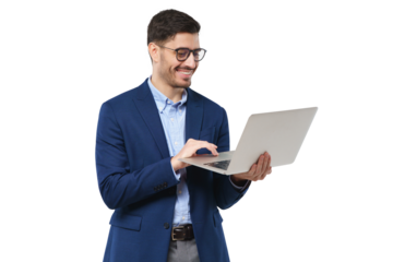 Young businessman wearing blue suit, standing with open laptop in hands, surfing the internet with smile, typing text