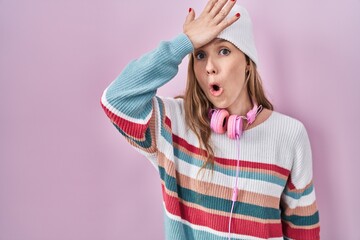 Young blonde woman standing over pink background surprised with hand on head for mistake, remember...