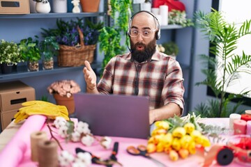 Young hispanic man with beard and tattoos working at florist shop doing video call scared and...