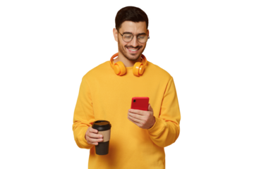 Young man in glasses, enjoying messages from friends via phone screen, smiling happily, drinking coffee, headphones round neck