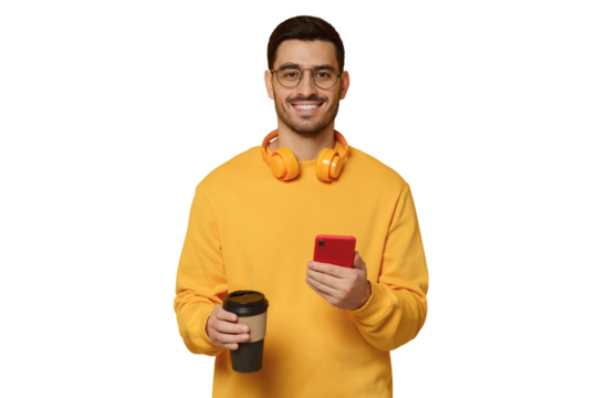 Young smiling man wearing yellow wireless headphones, holding takeaway coffee cup in one hand and phone in another