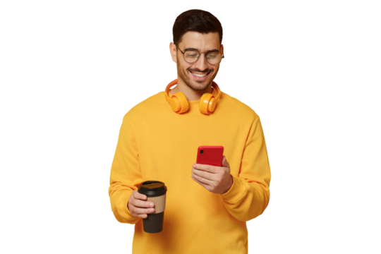 Young man in glasses, enjoying messages from friends via phone screen, smiling happily, drinking coffee, headphones round neck