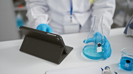 Fototapeta premium Woman scientist's hands expertly measuring liquid in test tube at lab, engaging in serious research with touchpad at her disposal