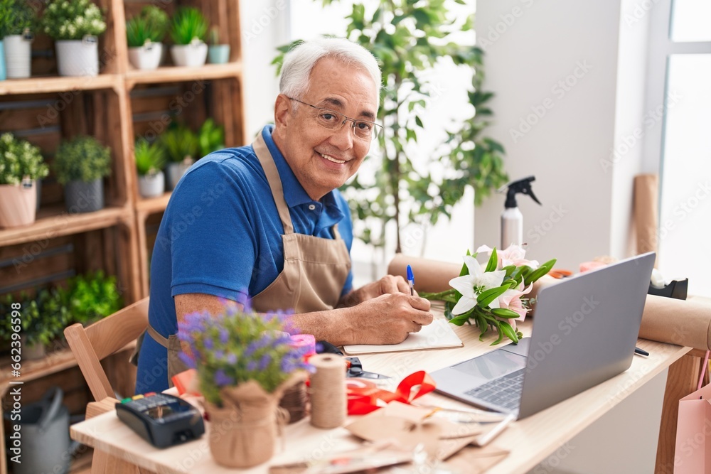 Sticker middle age grey-haired man florist using laptop writing on notebook at florist