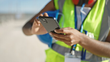 African american woman builder using smartphone at street