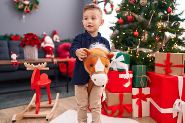 Adorable hispanic boy playing with horse toy standing by christmas tree at home