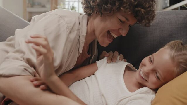 Slowmo of Caucasian woman with curly hair having fun tickling her preteen daughter