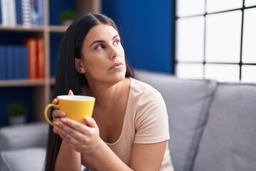Young beautiful hispanic woman drinking coffee with serious expression at home