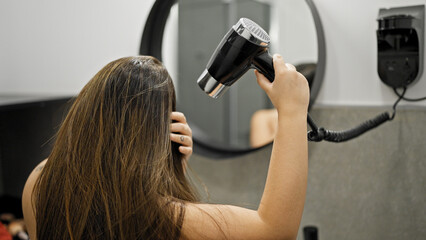 Young beautiful hispanic woman using hair dryer in the bathroom