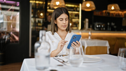 Young beautiful hispanic woman smiling happy using smartphone sitting on the table at the restaurant