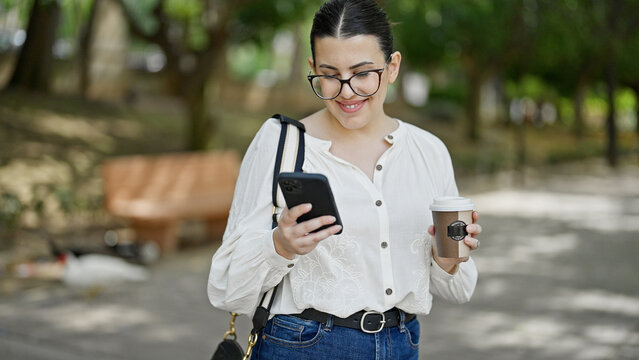 Young beautiful hispanic woman using smartphone drinking take away coffee at the park