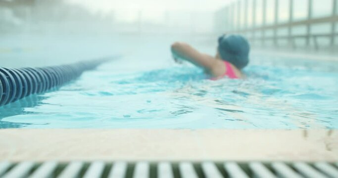 Portrait of beautiful woman relaxing on water in foggy smoky swimming pool, slow motion, back rare view Blurred background, sportswoman working out, preparing for competition