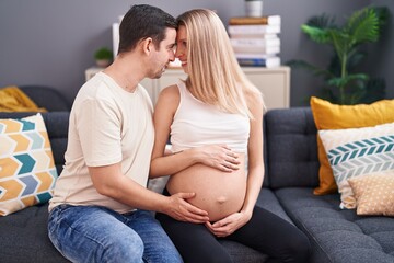 Man and woman couple touching belly sitting on sofa at home