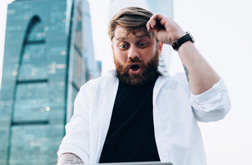 Joyful shocked man watching laptop in street