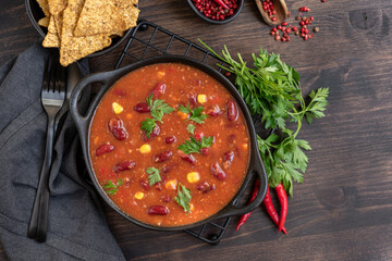 Bean and corn soup or ragout, red bean stew with corn chips nachos on a wooden background. Food Protein Vegan dish. Mexican food chili con carne with corn chips nachos. kidney bean